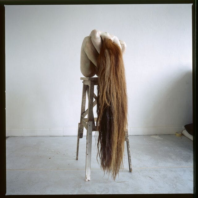 Work by Berlinde de Bruyckere , figure sits on a high stool with long hair