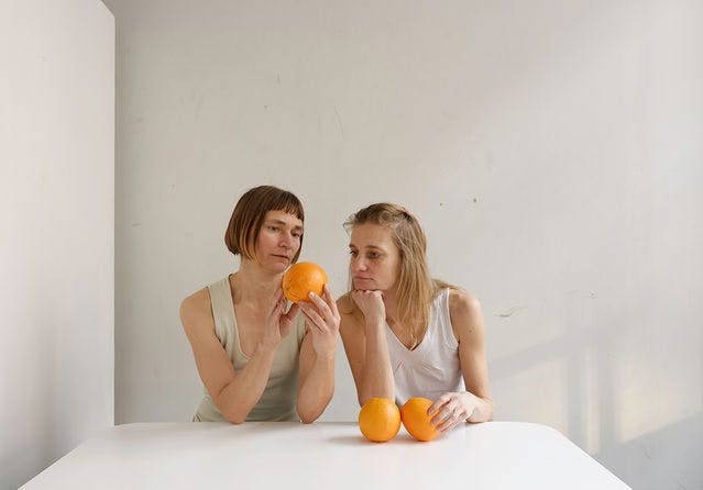 A photograph by Elina Brotherus showing two people looking at three oranges